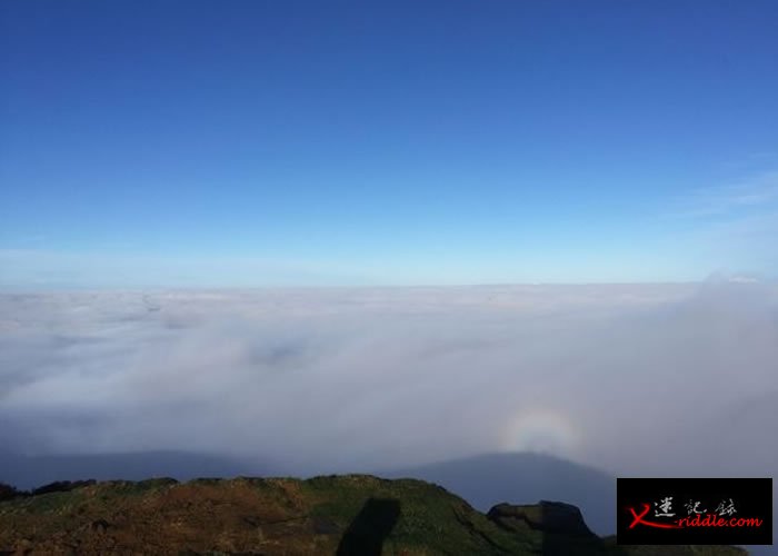 蓝天下山间被浓雾覆盖，彩虹光环罩住的人影屹立在山脊。